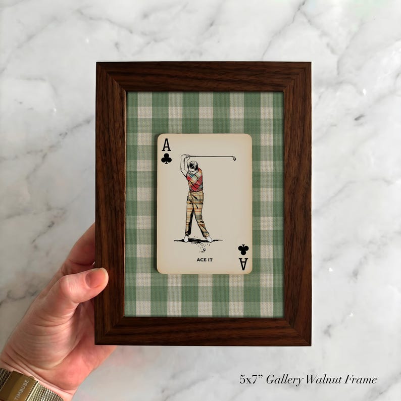 K&ouml;nnte beinhalten: Ein 13x18 cm gro&szlig;er Bilderrahmen aus dunklem Walnussholz mit einer Spielkarte, die einen Golfspieler beim Abschlag zeigt. Die Karte tr&auml;gt den Text ACE IT und den Buchstaben A mit einem Kreuz-Symbol. Der Hintergrund ist ein gr&uuml;n-wei&szlig;es Vichy-Muster.