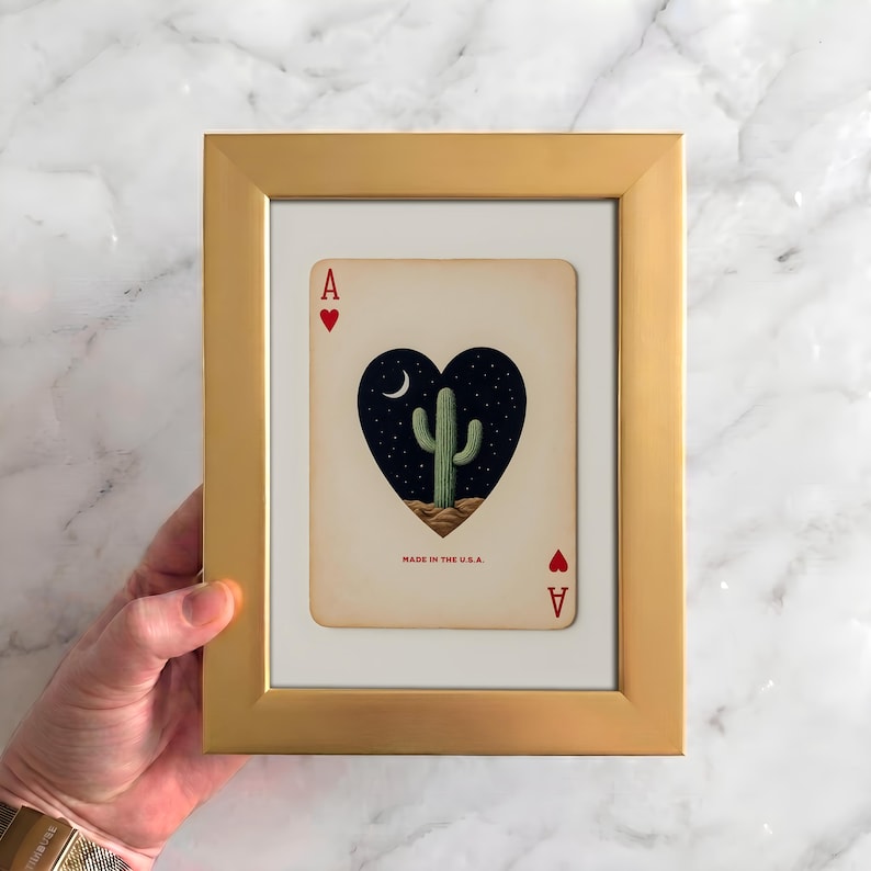 May include: A framed playing card featuring a heart-shaped design with a cactus under a crescent moon and stars. The card is an Ace of Hearts, set in a gold frame. The text "MADE IN THE U.S.A." is visible.
