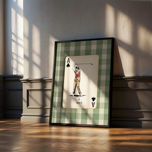 K&ouml;nnte beinhalten: Ein gerahmter Kunstdruck mit einem Kreuz-Ass-Spielkartendesign. Die Karte zeigt einen Golfer in einem roten Hemd und einer karierten Hose, der einen Schl&auml;ger schwingt, mit dem Text ACE IT. Der Hintergrund ist ein gr&uuml;n-wei&szlig;es Karomuster.