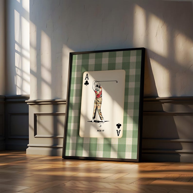K&ouml;nnte beinhalten: Ein gerahmter Kunstdruck mit einem Kreuz-Ass-Spielkartendesign. Die Karte zeigt einen Golfer in einem roten Hemd und einer karierten Hose, der einen Schl&auml;ger schwingt, mit dem Text ACE IT. Der Hintergrund ist ein gr&uuml;n-wei&szlig;es Karomuster.