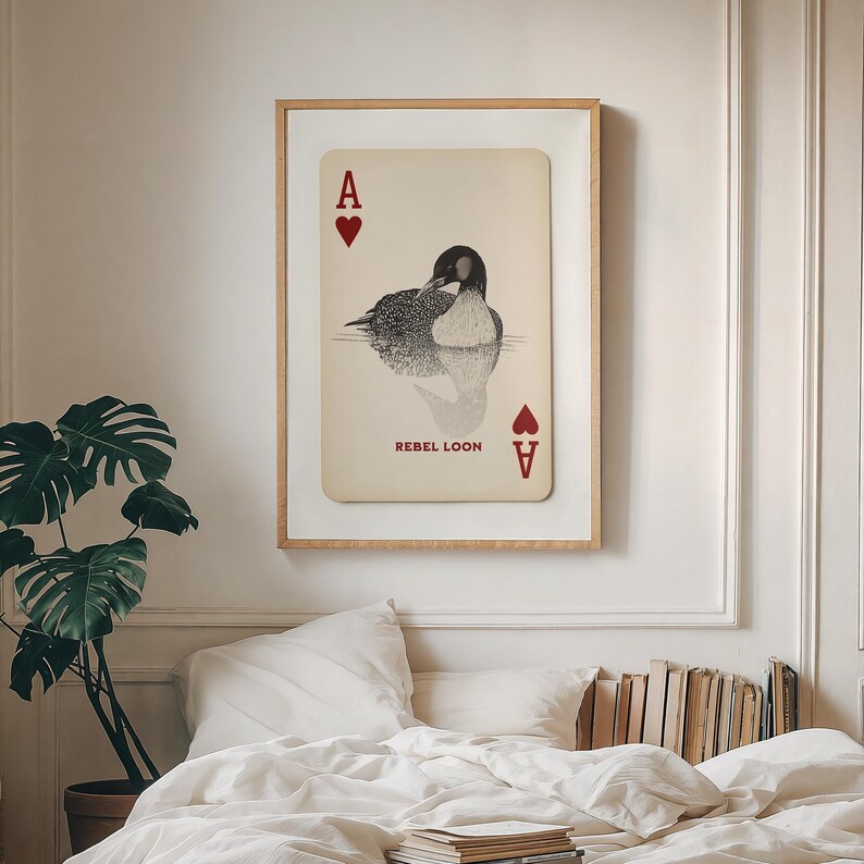 Puede incluir: Una l&aacute;mina de arte mural enmarcada con un dise&ntilde;o de carta de juego color crema y una ilustraci&oacute;n en blanco y negro de un colimbo nadando en el agua. La carta muestra la letra A y un coraz&oacute;n rojo, con el texto REBEL LOON debajo.