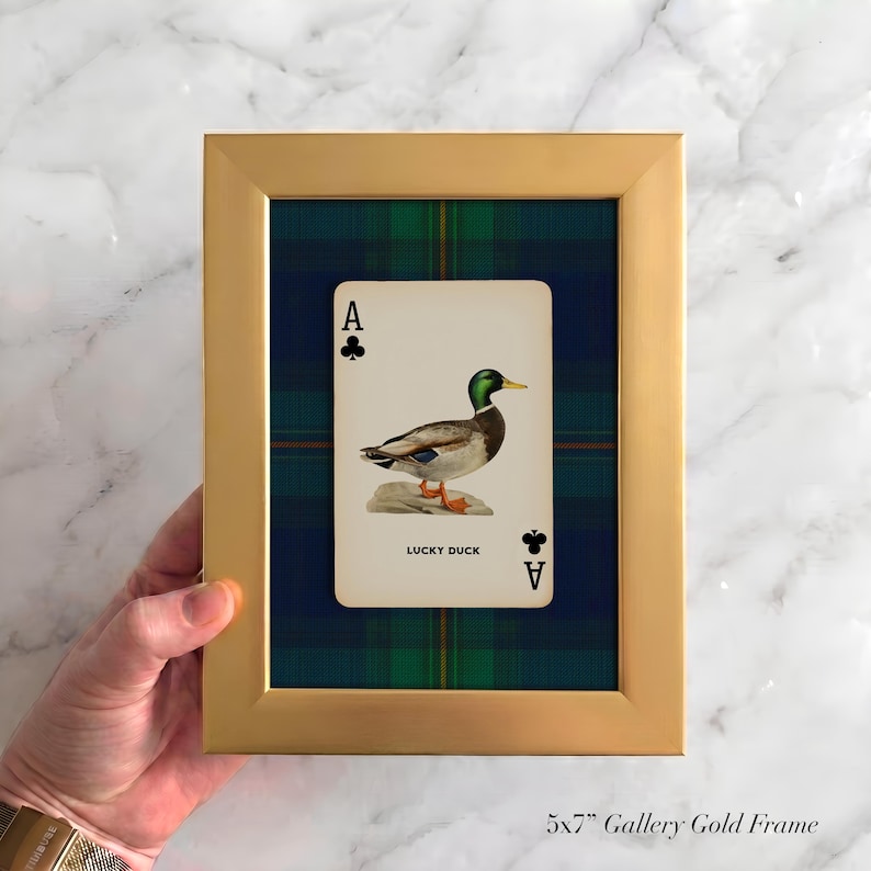 May include: A gold framed print featuring an Ace of Clubs playing card with a duck illustration. The card is set against a blue and green plaid background. The text "LUCKY DUCK" is visible on the card.