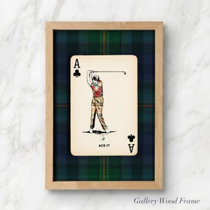 May include: Framed artwork featuring a playing card with a golf theme. The card is the Ace of Clubs, with a golfer in mid-swing. The background is a green and blue plaid pattern, and the frame is light wood. The text "ACE IT" is at the bottom.