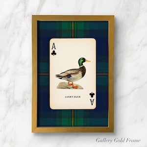 May include: A framed print featuring a playing card with an illustration of a duck. The card is the Ace of Clubs, with the text "LUCKY DUCK" below the duck image. The frame is gold, and the background is a blue and green plaid pattern.
