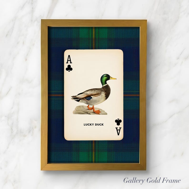May include: A framed print featuring a playing card with an illustration of a duck. The card is the Ace of Clubs, with the text "LUCKY DUCK" below the duck image. The frame is gold, and the background is a blue and green plaid pattern.