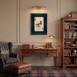 May include: A framed print of a playing card featuring a duck illustration, set against a green and blue plaid background. The card is labeled "Lucky Duck" and is displayed above a wooden desk and chair, creating a cozy, traditional aesthetic.