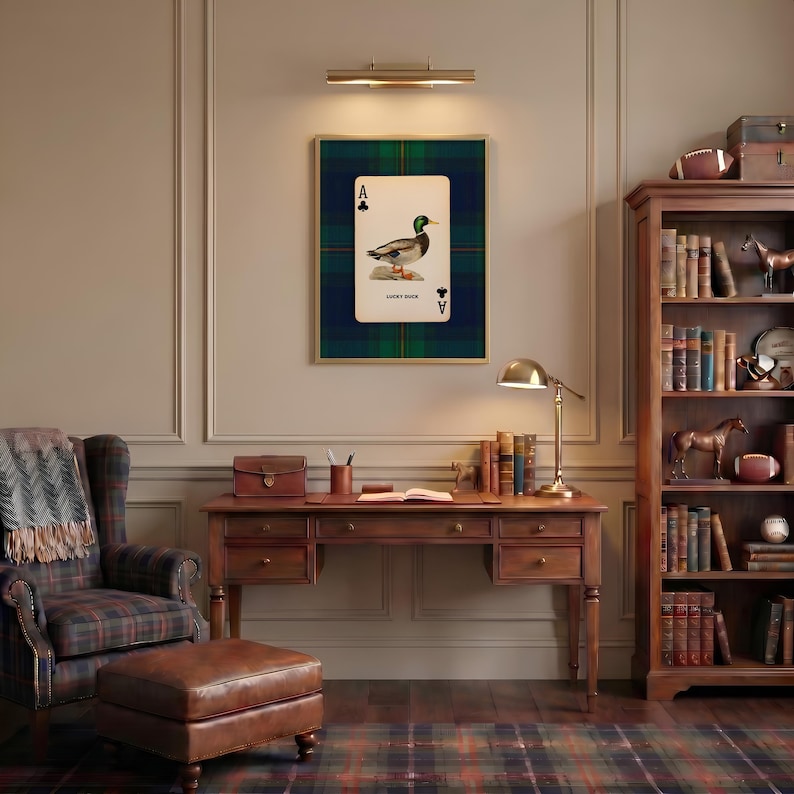 May include: A framed print of a playing card featuring a duck illustration, set against a green and blue plaid background. The card is labeled "Lucky Duck" and is displayed above a wooden desk and chair, creating a cozy, traditional aesthetic.