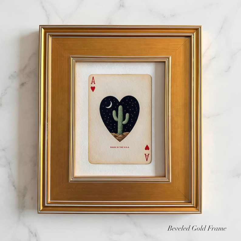 May include: Framed playing card art featuring the Ace of Hearts. The card displays a heart-shaped night scene with a cactus, moon, and stars. The card is framed in a gold beveled frame.