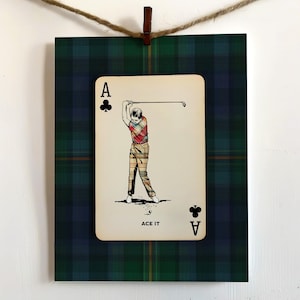 May include: A framed print featuring a playing card with a golfer illustration. The card is the Ace of Clubs, with the text "ACE IT" below the image. The background is a green and blue plaid pattern.