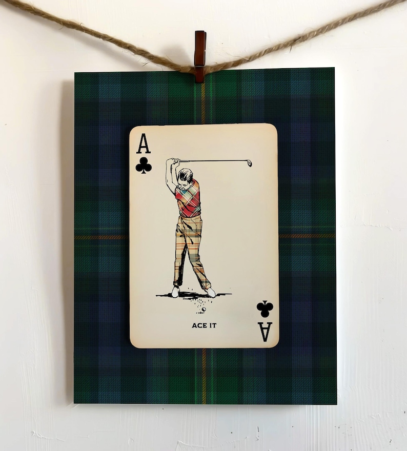 May include: A framed print featuring a playing card with a golfer illustration. The card is the Ace of Clubs, with the text "ACE IT" below the image. The background is a green and blue plaid pattern.