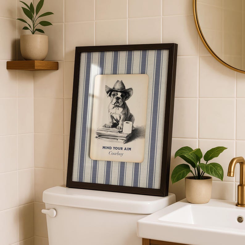 May include: Framed artwork featuring a bulldog wearing a cowboy hat, resting on books and a roll of toilet paper. The artwork is set against a blue and white striped background, with the text "MIND YOUR AIM Cowboy".