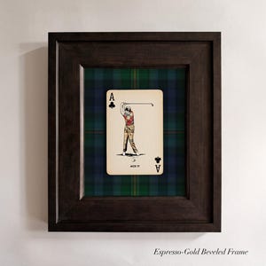 May include: Framed artwork featuring a playing card with a golfer illustration. The card is set against a green, blue, and black plaid background, within a dark brown beveled frame. The card reads "ACE IT".