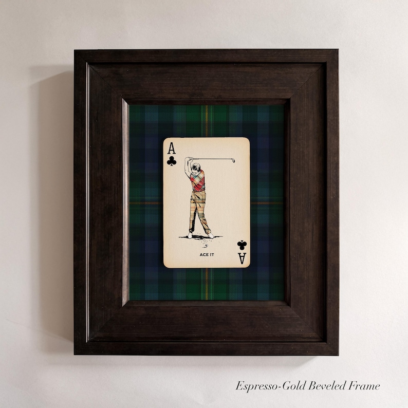 May include: Framed artwork featuring a playing card with a golfer illustration. The card is set against a green, blue, and black plaid background, within a dark brown beveled frame. The card reads "ACE IT".