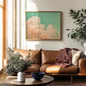 Panoramic wall art featuring billowing pink clouds against a soft sage green sky, creating airy Western big-sky artwork ideal for farmhouse, ranch, or modern bedroom décor. Shown finished as a natural wood framed giclée print.