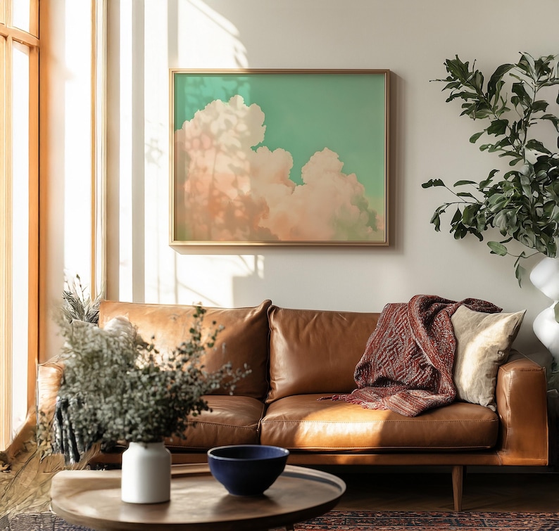 Panoramic wall art featuring billowing pink clouds against a soft sage green sky, creating airy Western big-sky artwork ideal for farmhouse, ranch, or modern bedroom décor. Shown finished as a natural wood framed giclée print.