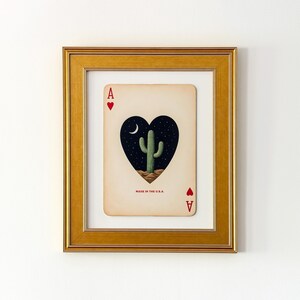 May include: Framed art print of the Ace of Hearts playing card. The card features a heart-shaped design with a cactus under a crescent moon and stars. The text "MADE IN THE U.S.A." is printed at the bottom.