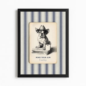 May include: Framed artwork featuring a bulldog wearing a cowboy hat, sitting on books with a roll of toilet paper. The artwork has the text "MIND YOUR AIM Cowboy" in a black frame with a blue and white striped background.