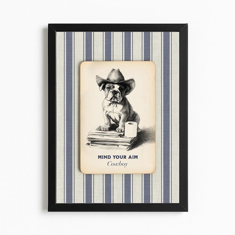 May include: Framed artwork featuring a bulldog wearing a cowboy hat, sitting on books with a roll of toilet paper. The artwork has the text "MIND YOUR AIM Cowboy" in a black frame with a blue and white striped background.