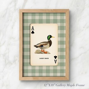 May include: A 12-inch by 18-inch maple wood frame containing a print of an ace of clubs playing card featuring a mallard duck illustration and the text LUCKY DUCK. The background behind the card is a light green and white gingham fabric pattern.