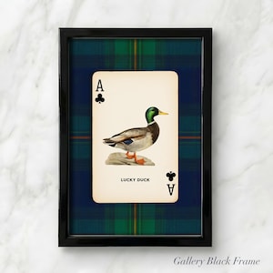 May include: A framed print featuring a playing card with an illustration of a duck. The card is set against a blue and green plaid background within a black frame. The card reads "LUCKY DUCK" and has the Ace of Clubs.
