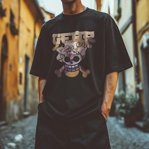 May include: Black t-shirt with a graphic of a skull and crossbones with the word "GEAR" above it. The skull has a purple and gold design. The shirt is oversized and has short sleeves.