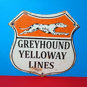 May include: A shield-shaped metal sign featuring an orange upper section with a white running greyhound silhouette and a white lower section with the black text GREYHOUND YELLOWAY LINES. The sign has visible rust along the edges and mounting holes.