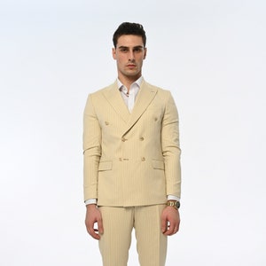 Men's suit consisting of cream, double-breasted, pointed wide collar, pin stripe, decorative gold buttons, slim fit trousers and jacket represents not only elegance but also sophisticated elegance with its cream colour and double-breasted design.