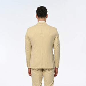 Men's suit consisting of cream, double-breasted, pointed wide collar, pin stripe, decorative gold buttons, slim fit trousers and jacket represents not only elegance but also sophisticated elegance with its cream colour and double-breasted design.