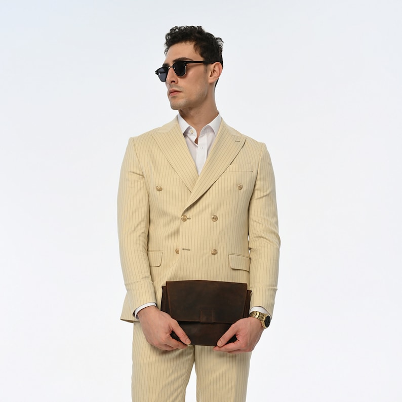 Men's suit consisting of cream, double-breasted, pointed wide collar, pin stripe, decorative gold buttons, slim fit trousers and jacket represents not only elegance but also sophisticated elegance with its cream colour and double-breasted design.