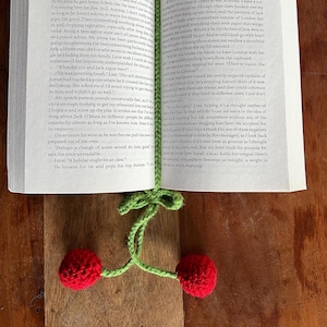 May include: Close-up of an open book with a green, red, and white crocheted cherry bookmark. The book is open to a page with text about a character named Jack and a character named Sarah.