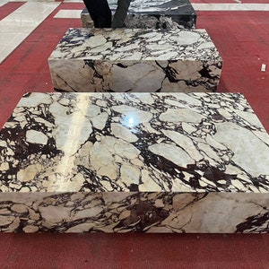 May include: Two large rectangular marble slabs with a white background and black and brown veining. The slabs are sitting on a red surface.