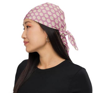 May include: A woman wearing a pink and white polka dot bandana tied around her head. She is wearing a black shirt.