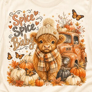 May include: A cream-colored t-shirt featuring a graphic of a fluffy highland cow wearing a knit beanie and plaid scarf. The design includes pumpkins, a vintage orange truck, butterflies, and the text Spice Spice Baby in plaid lettering.