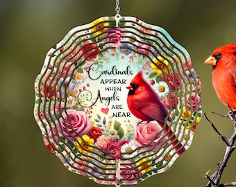 Könnte beinhalten: Ein mehrschichtiger, kreisförmiger Windspinner mit einem leuchtend roten Kardinal, der auf einem Blumendesign mit Rosen und Gänseblümchen sitzt. Der Text lautet: "Kardinäle erscheinen, wenn Engel in der Nähe sind."
