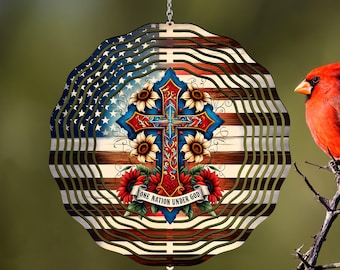 Könnte beinhalten: Ein mehrschichtiger Holz-Windspinner mit einem Design der amerikanischen Flagge, einem Kreuz, Sonnenblumen und dem Text "ONE NATION UNDER GOD". Ein leuchtend roter Kardinal sitzt rechts auf einem Ast.