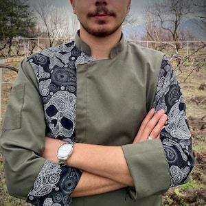 May include: A green chef jacket with black and white paisley skull print on the sleeves and collar. The jacket has a mandarin collar and a single button closure.