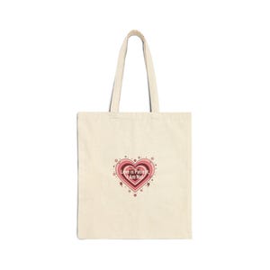 May include: Cream tote bag featuring a layered pink and red heart design with the text "Love is Patient, I Am Not". The bag has long handles and is made of a light-colored fabric.