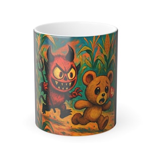 Puede incluir: Taza de cerámica blanca con una colorida ilustración de un diablo rojo con un tridente persiguiendo a un oso de peluche marrón por un campo de maíz. La taza tiene un acabado brillante y un interior blanco.