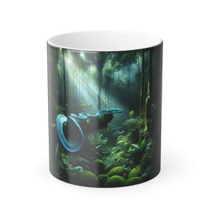 Könnte beinhalten: Weißer Keramikbecher mit einer Dschungelszene mit einer blauen Schlange. Das Design umfasst grünes Laub, Bäume und Sonnenlicht. Der Becher ist zylindrisch und für heiße Getränke geeignet.