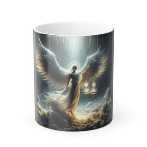 May include: A white ceramic coffee mug featuring a celestial design. The artwork depicts an angel with large white wings, holding scales and a staff, set against a backdrop of clouds and light. The mug has a black exterior and a white interior.