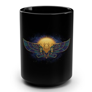 May include: Black ceramic mug featuring a colorful Egyptian-inspired design. The design includes a golden sun, a scarab beetle, and detailed wings in shades of blue, green, and gold. The mug is cylindrical and has a glossy finish.