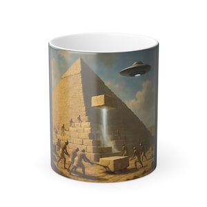 May include: White ceramic mug featuring a surreal illustration of the pyramids with a UFO hovering above. The image depicts figures moving blocks, with a beam of light emanating from the pyramid. The mug has a glossy finish.