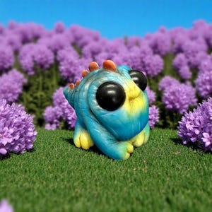 Op de afbeelding: Een klein, blauw en geel dinosaurusbeeldje met grote zwarte ogen. Het beeldje staat op een bed van groen gras met paarse bloemen op de achtergrond.