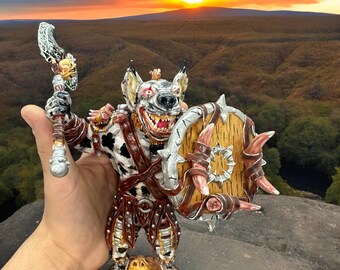 May include: A hand-painted figurine of a hyena warrior holding a spear and a shield. The figurine is painted in shades of white, brown, and black, with silver accents. The hyena is wearing a leather armor and has a fierce expression on its face.