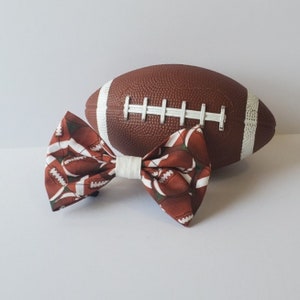 May include: A brown and white bow tie with a football pattern. The bow tie is next to a brown and white football.