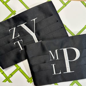 May include: Two black satin fabric belts with white embroidered initials. The first belt has the initials "ZT" and "Y" embroidered on it. The second belt has the initials "ML" and "P" embroidered on it.
