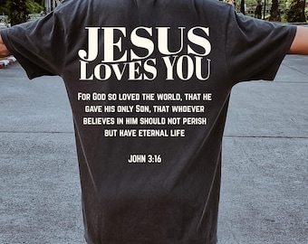 May include: Dark gray t-shirt with the text "JESUS LOVES YOU" in white block letters. Below the text is a Bible verse from John 3:16. The shirt is a casual style, suitable for everyday wear.