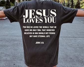 May include: Dark gray t-shirt with the text "JESUS LOVES YOU" in white block letters. Below the text is a Bible verse from John 3:16. The shirt is a casual style, suitable for everyday wear.