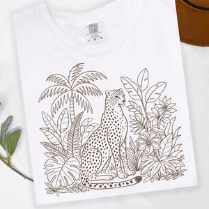 May include: White t-shirt featuring a brown illustration of a cheetah in a jungle setting. The shirt has a crew neck and the word "WHITE" is at the top left. The tag reads "COMFORT COLORS" and the size is L-G-G.