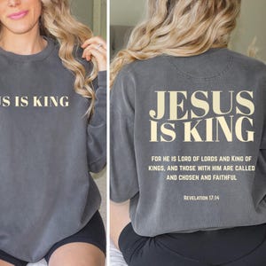 May include: A charcoal gray sweatshirt with the text "JESUS IS KING" printed in a cream color on the front and back. The back also features a Bible verse. A comfortable, casual top.